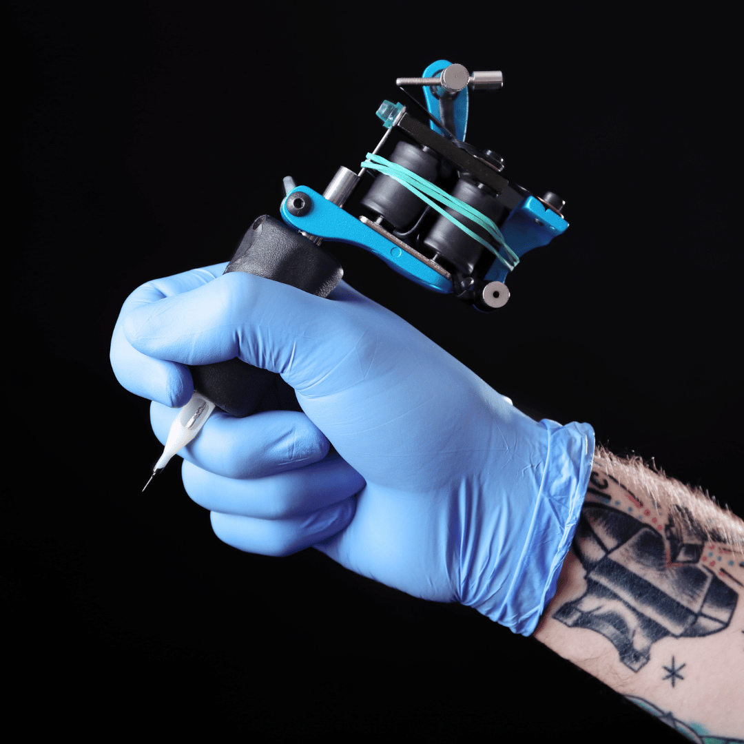 Tatuador trabajando con guantes de nitrilo azul sin polvo, ofreciendo seguridad e higiene durante largas sesiones de tatuaje en estudio de Gran Canaria.