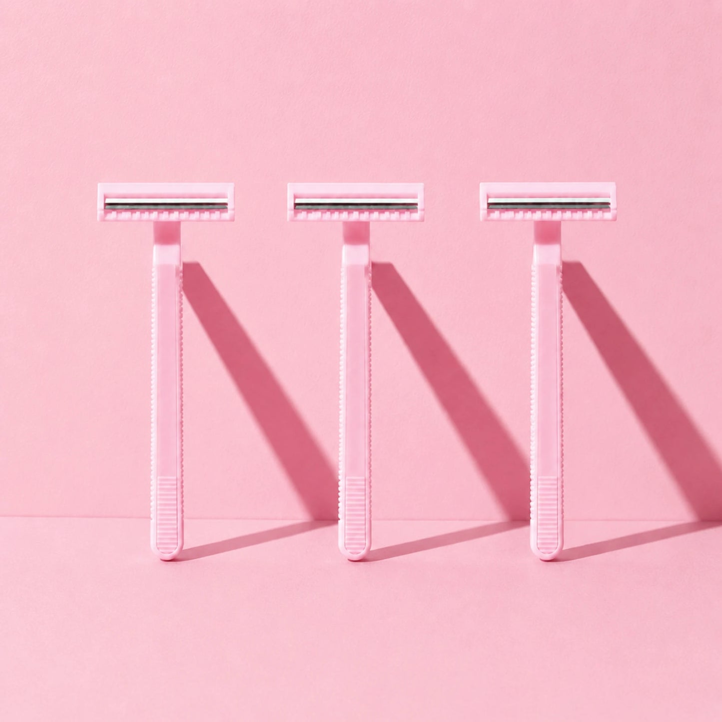 Tres Rasuradoras Desechables de 2 Hojas rosas en una composición de estudio sobre fondo rosa