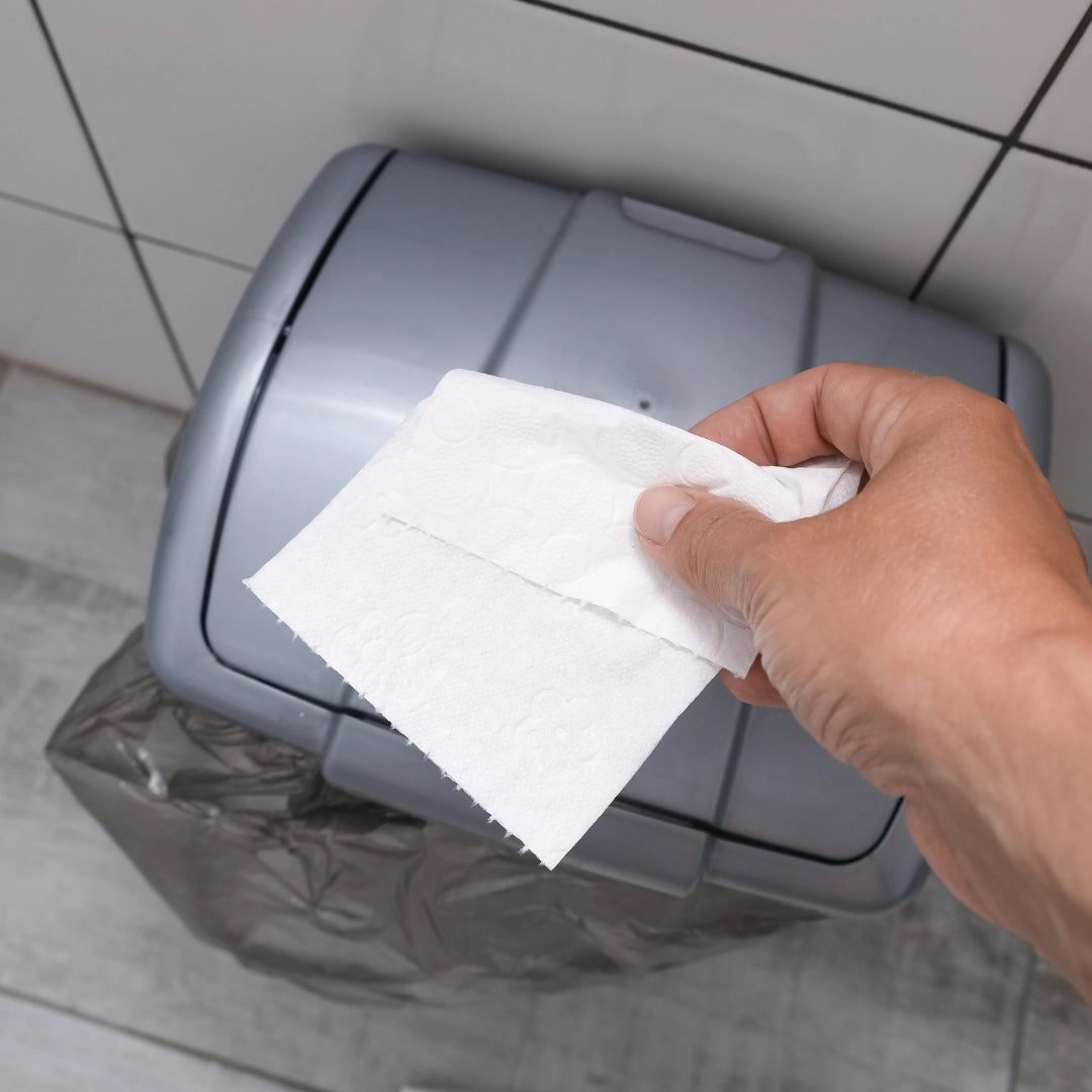 Persona tirando papel higiénico en una papelera pequeña de baño con bolsa de basura en Gran Canaria.