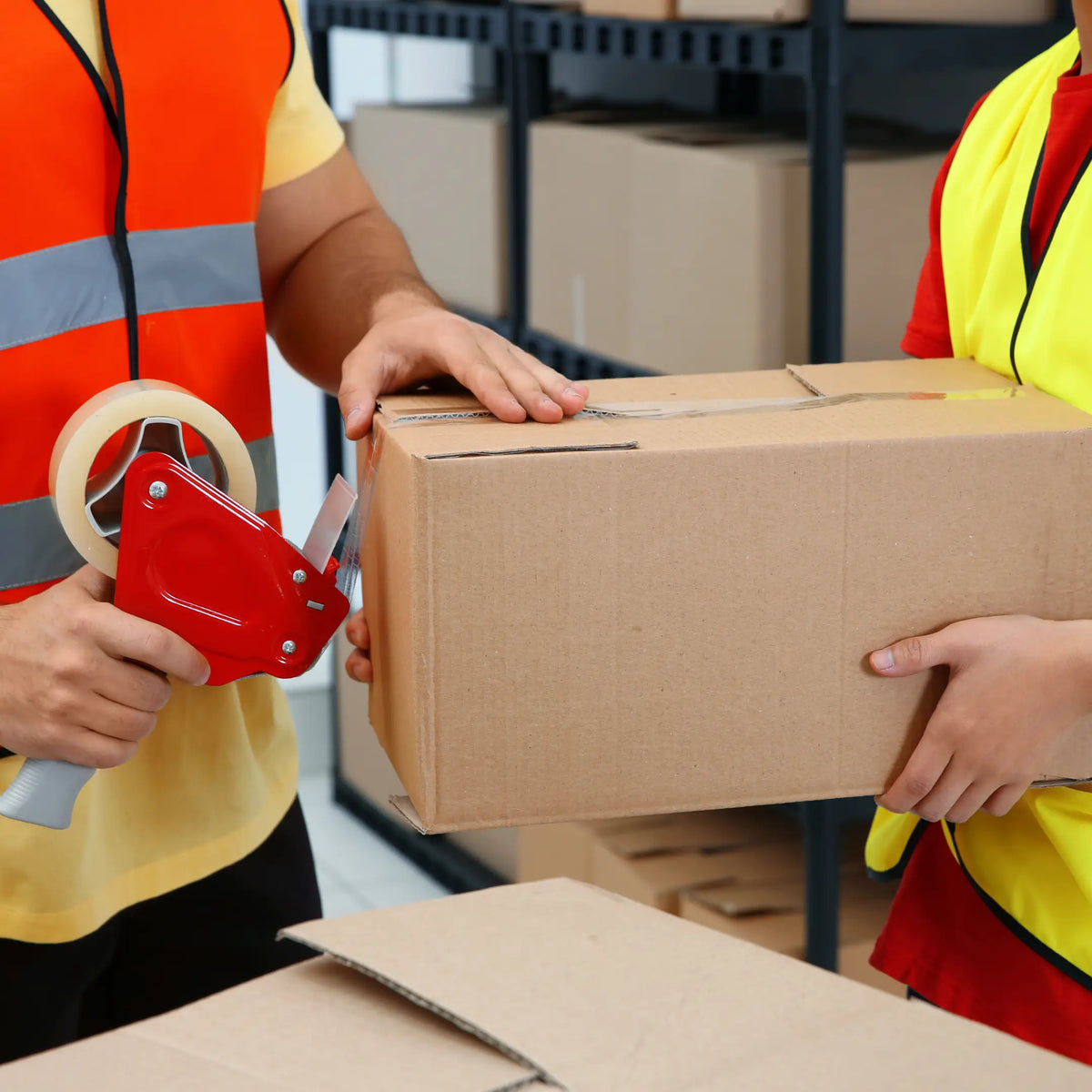 Trabajadores de almacén cerrando una caja con cinta de embalar y dispensador profesional en Gran Canaria.