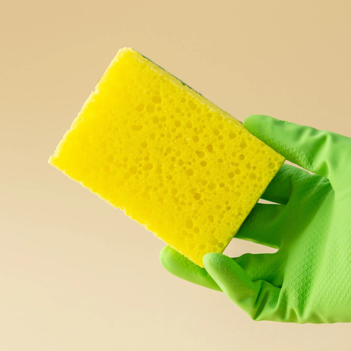 Mano protegida con guante sujetando un estropajo esponja salvauñas para el lavado y limpieza de vajilla utilizando los productos lavavajillas de DMP en Gran Canaria.