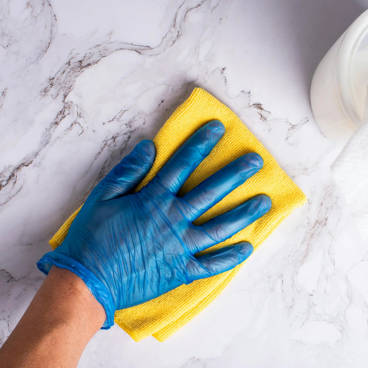 Mano protegida con guante de nitrilo azul limpiando una superficie con un paño de microfibra durante una tarea de limpieza en Gran Canaria.