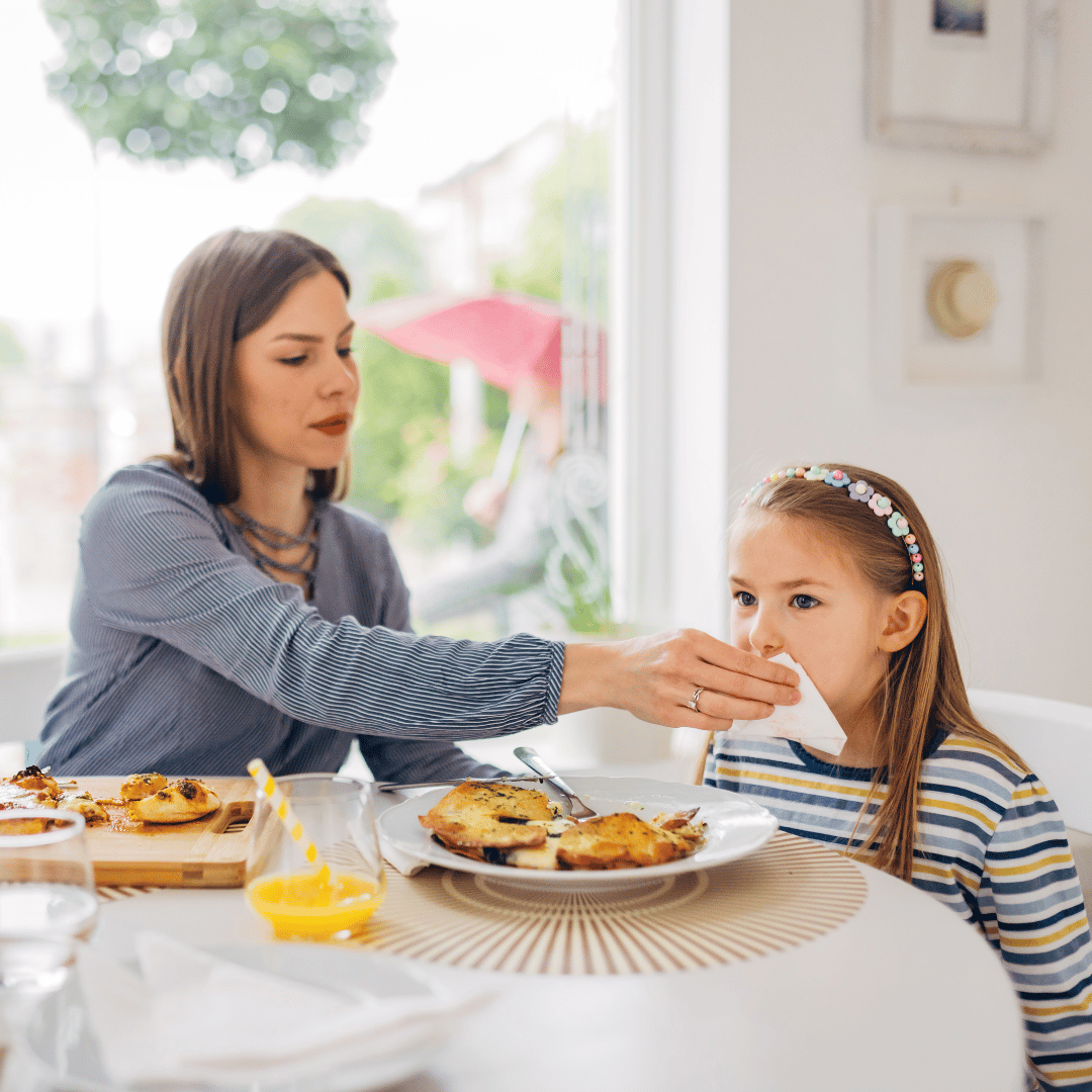 Madre limpiando la boca de su hija con servilleta de papel 40x40 blanca; servilleta resistente y absorbente apta para uso en cafeterías y restaurantes de Canarias.