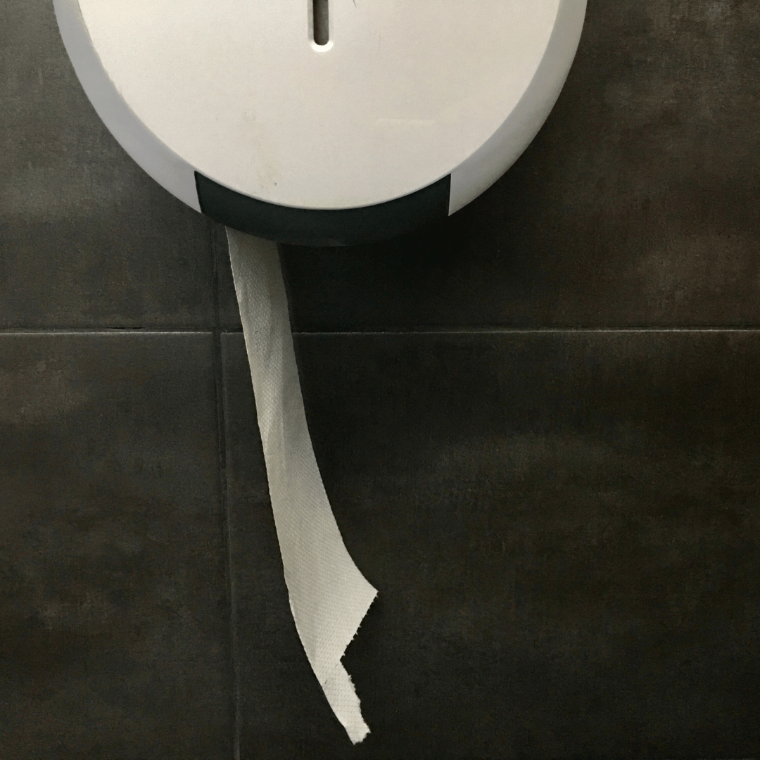 Papel higiénico industrial saliendo de portabobina de celulosa en baño público.