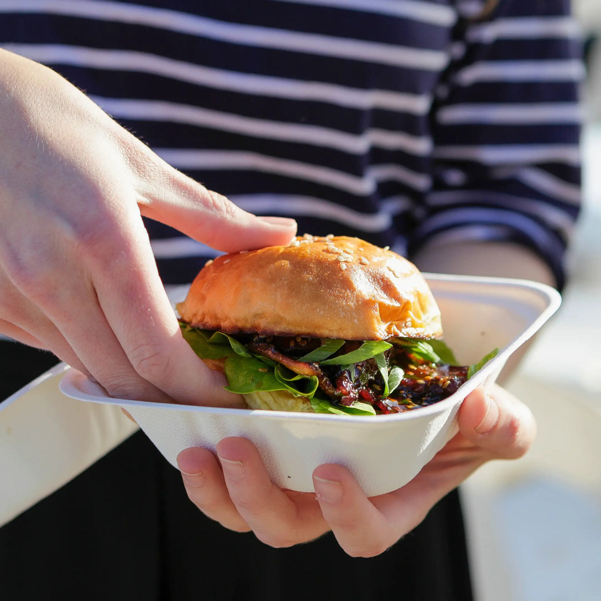 Persona sacando una hamburguesa caliente de un envase portamenú para comida Take Away en Gran Canaria.
