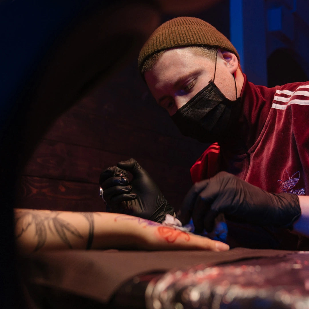 Tatuador utilizando una mascarilla quirúrgica negra Tipo IIR mientras realiza un trabajo profesional a un cliente en Gran Canaria